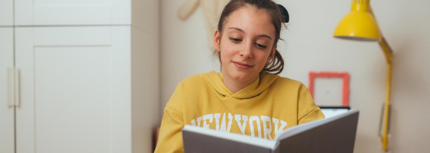 College student reading a book near a lamp. 
