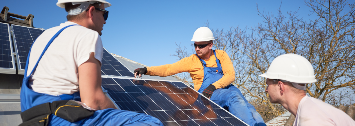 A group of three contractors installing solar panels on a residential roof.