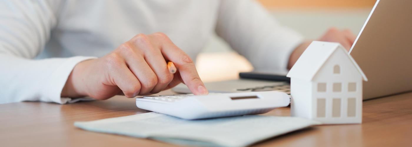 Woman using a calculator and a white house sitting on table next to it.